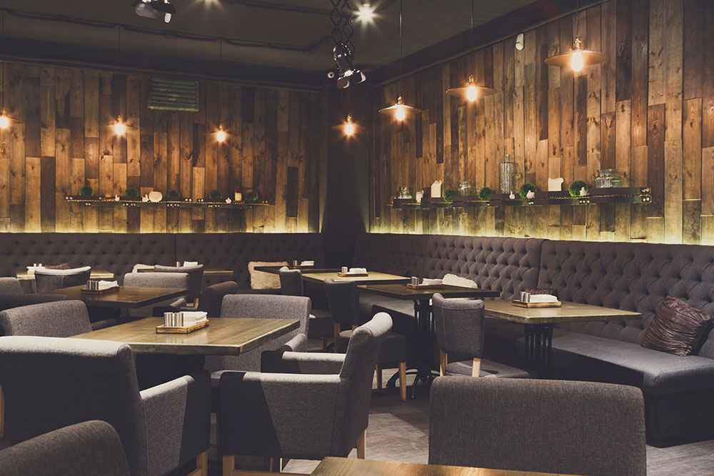 Modern restaurant with wood paneling on the walls, booths, and tables with chairs.